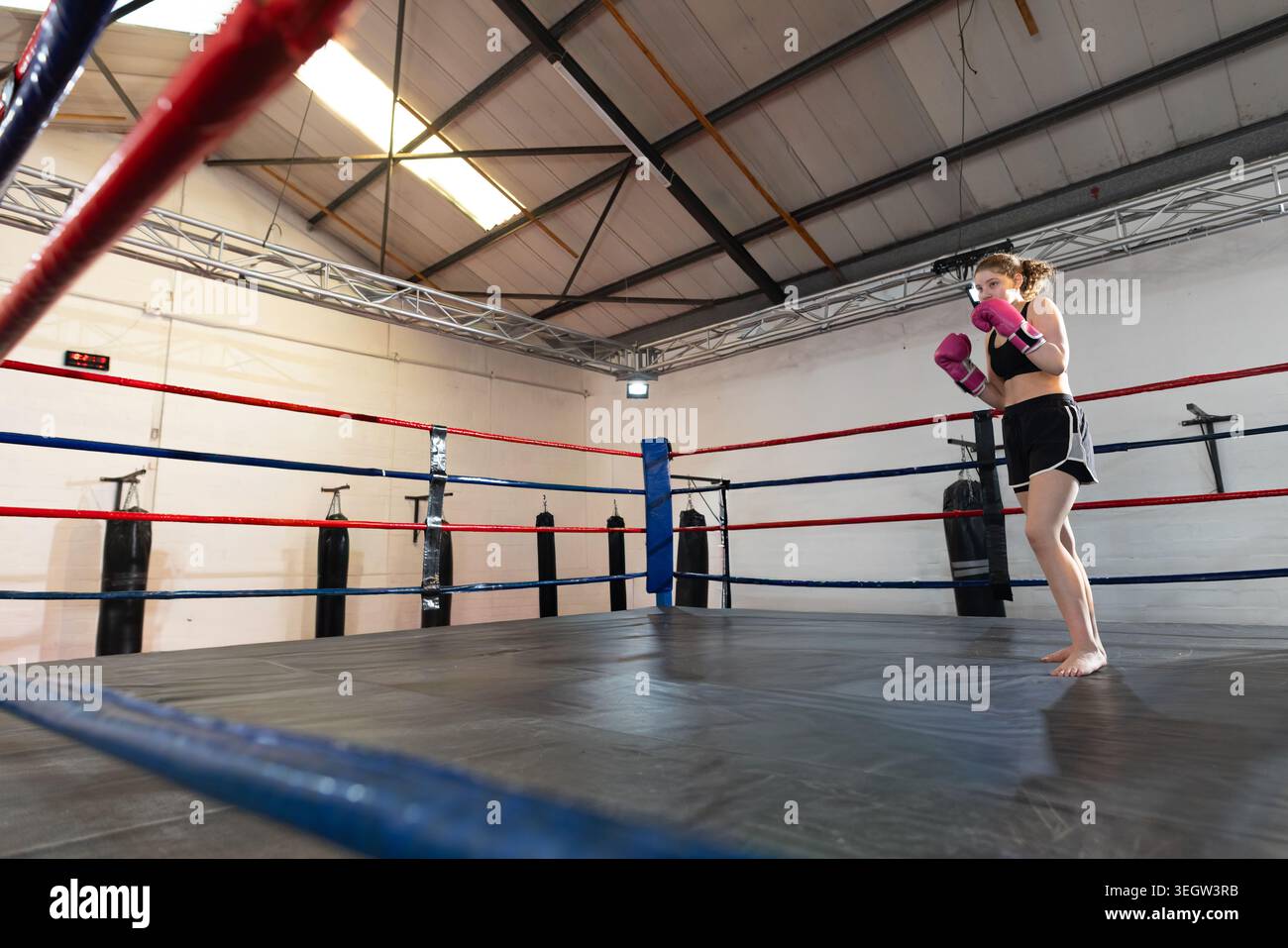 Boxeur adolescente debout sur la droite de l'anneau, pratiquant avec des gants roses, pieds nus, espace copie Banque D'Images