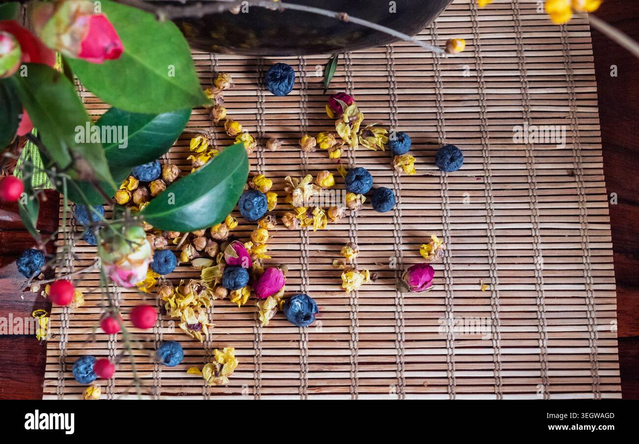 Fleurs et baies dispersées sur un tapis de bambou avec un vase noir sur une table en bois Banque D'Images
