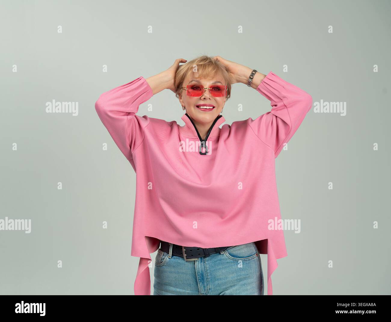 Une femme adulte, émotionnelle, espiègle, heureuse dans des vêtements roses et des lunettes avec ses mains levées Banque D'Images