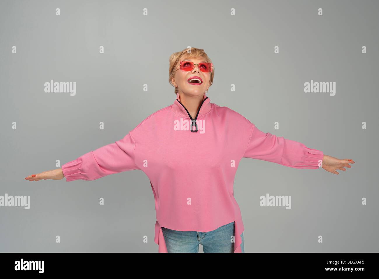 Une femme adulte, émotionnelle, espiègle, heureuse dans des vêtements roses et des lunettes avec ses mains levées Banque D'Images