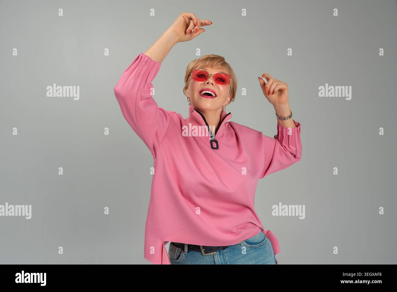 Une femme adulte, émotionnelle, espiègle, heureuse dans des vêtements roses et des lunettes avec ses mains levées Banque D'Images