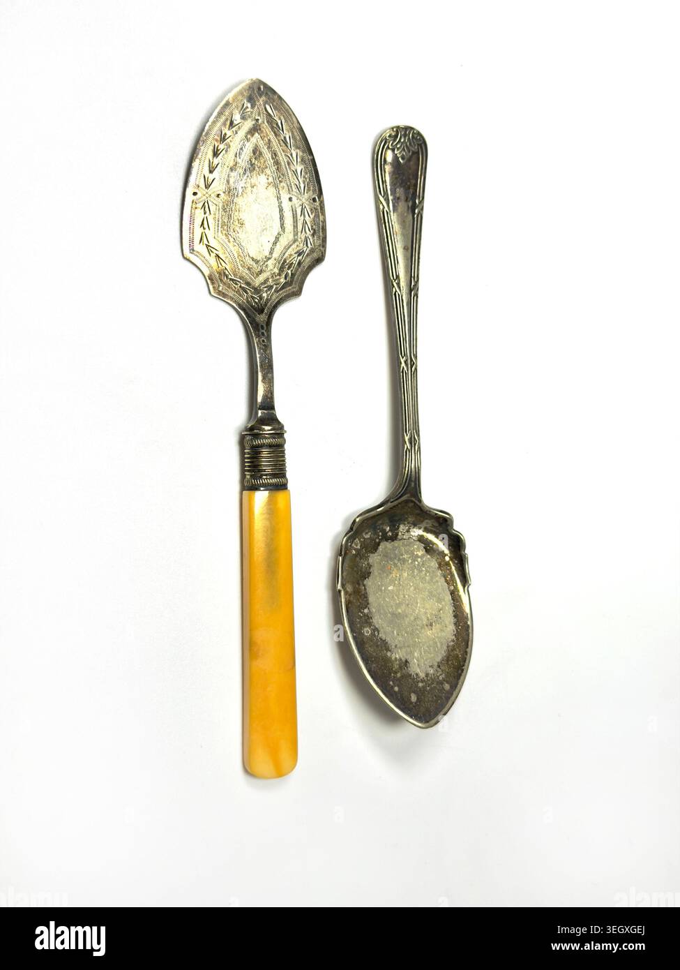 Deux cuillères en argent antique gravées ternies, ustensiles dont un serveur avec un manche jaune et une cuillère isolée sur fond blanc Banque D'Images