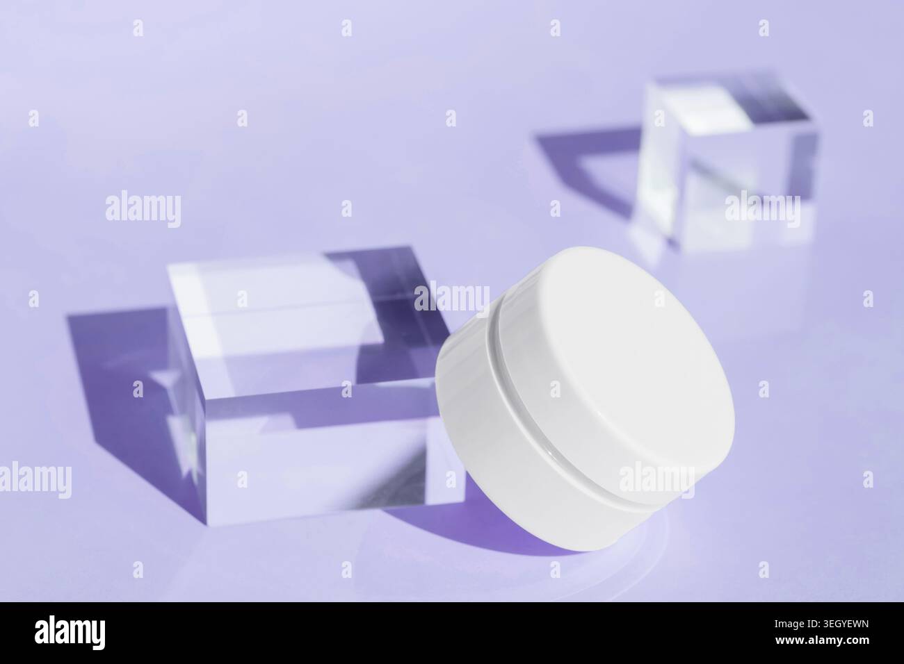 Pot de récipient de crème cosmétique et cubes de verre transparents sur fond violet, concept de produit de soin de la peau, présentation d'emballage de beauté de luxe Banque D'Images