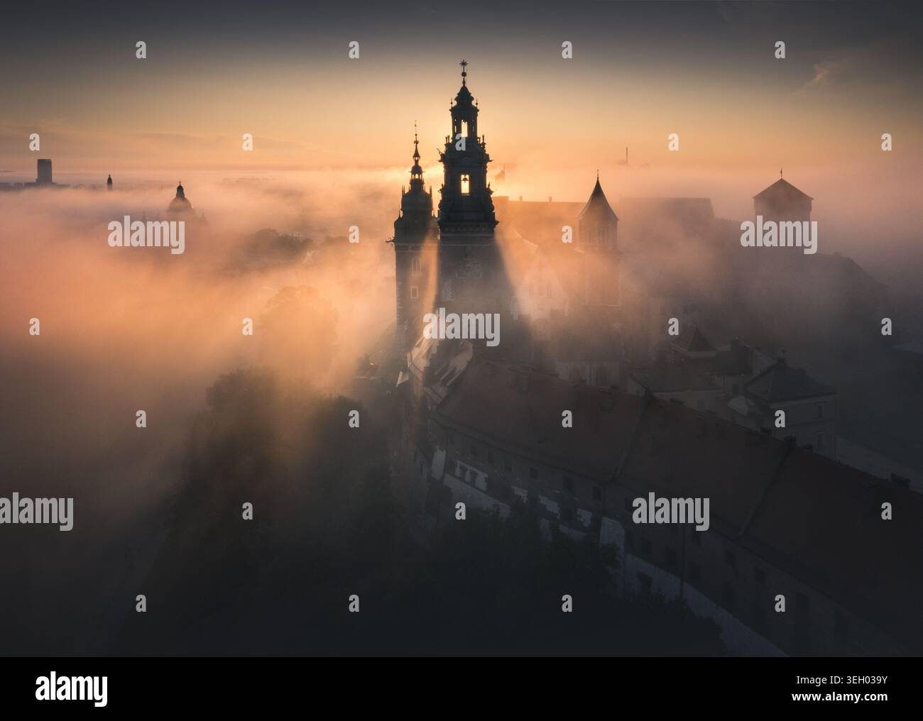 Vue aérienne du château royal de Wawel et de la cathédrale enveloppés dans un épais brouillard matinal lors d'un lever de soleil doré à Cracovie, petite Pologne Voïvodie, Pologne. Banque D'Images