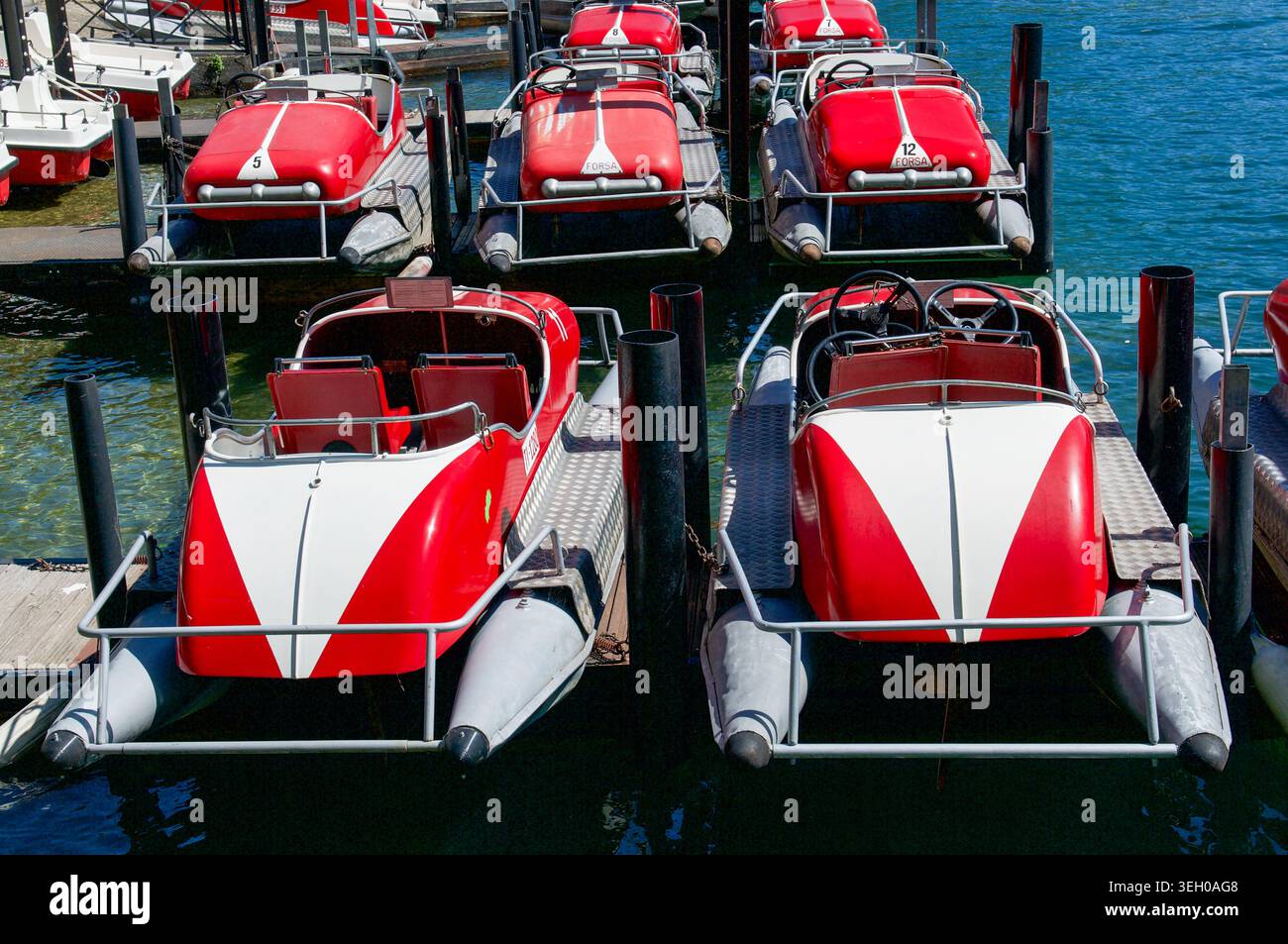 Rangée de bateaux à aubes rouges et blancs classiques ou pédalos amarrés à un quai sur l'eau bleue ensoleillée du lac de Lugano, Suisse. Banque D'Images