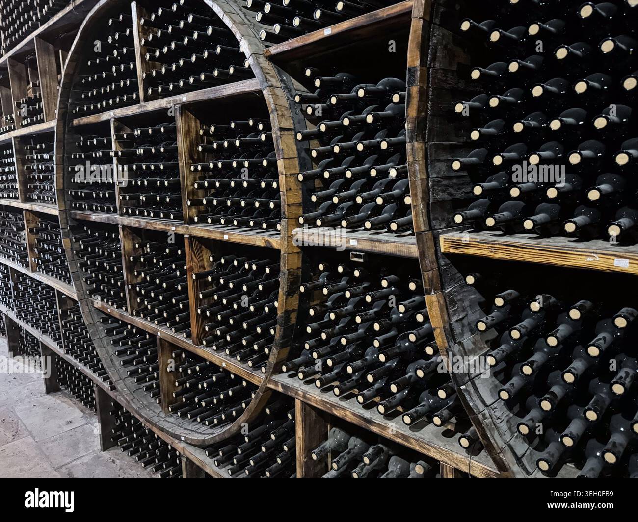 Rangées de bouteilles de vin foncées stockées horizontalement dans de grands supports rustiques en forme de tonneau en bois à l'intérieur d'une cave à vin ou d'une salle de stockage de cave à vin. Banque D'Images