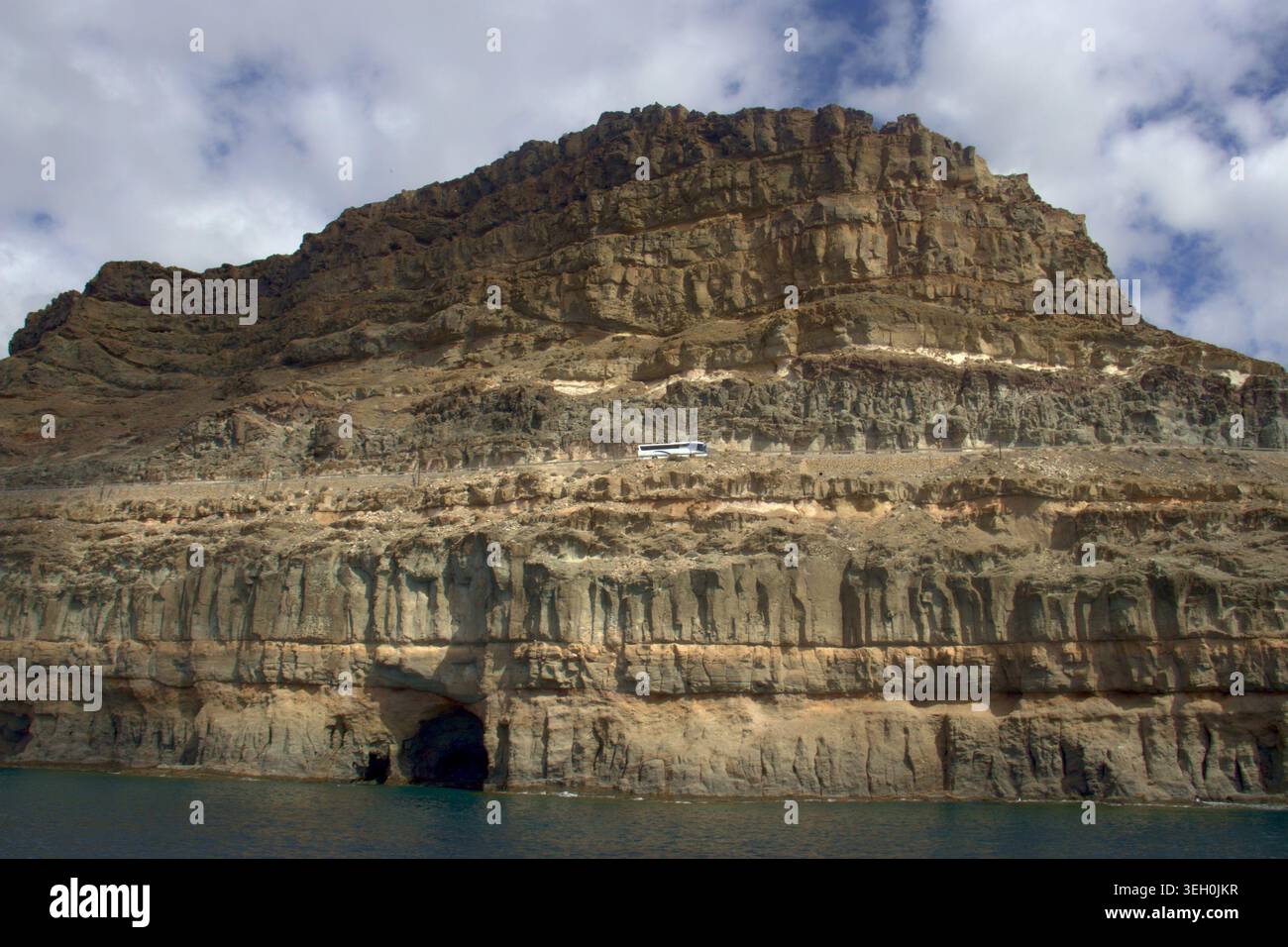 Une vue sous-jacente depuis l'eau montrant un bus touristique conduisant le long d'une autoroute pittoresque creusée dans d'énormes falaises volcaniques stratifiées. Banque D'Images