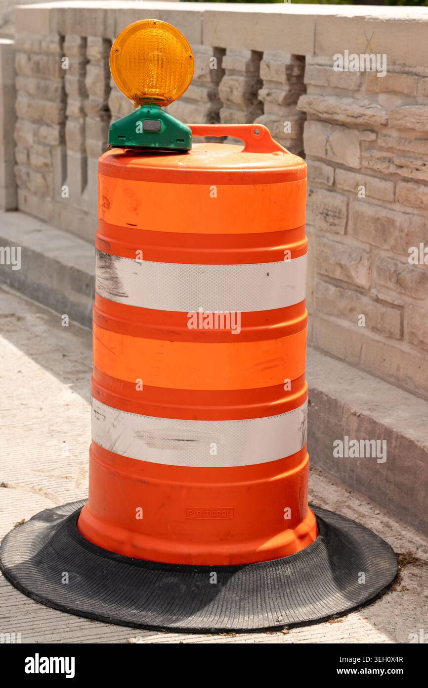 Tonneau de route orange avec deux bandes blanches réfléchissantes et une petite lumière ambre sur le dessus, utilisé pour délimiter les zones de construction et assurer la sécurité Banque D'Images