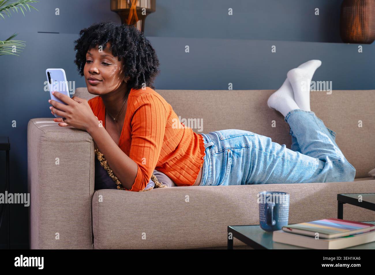 Femme allongée sur un canapé et utilisant son smartphone à la maison Banque D'Images