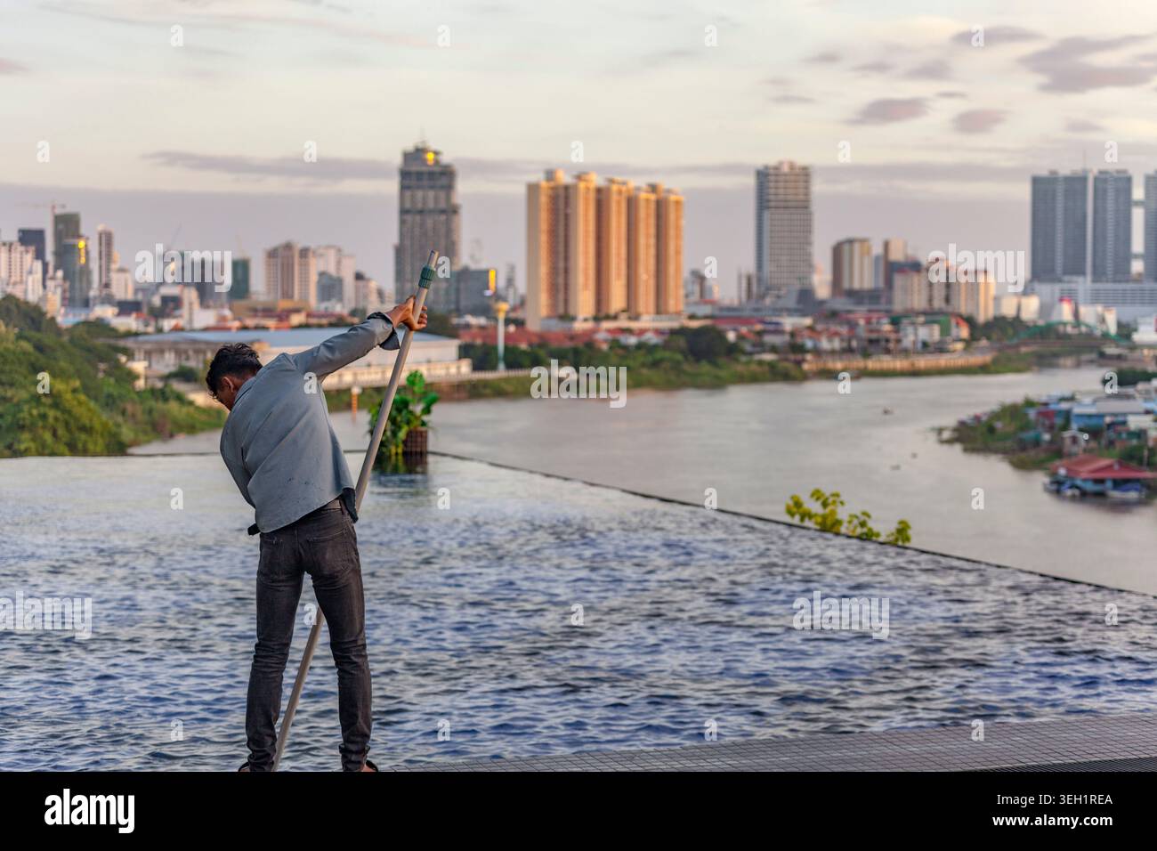 Homme nettoyant la piscine sur le toit à l'aube, Phnom Penh, Cambodge Banque D'Images