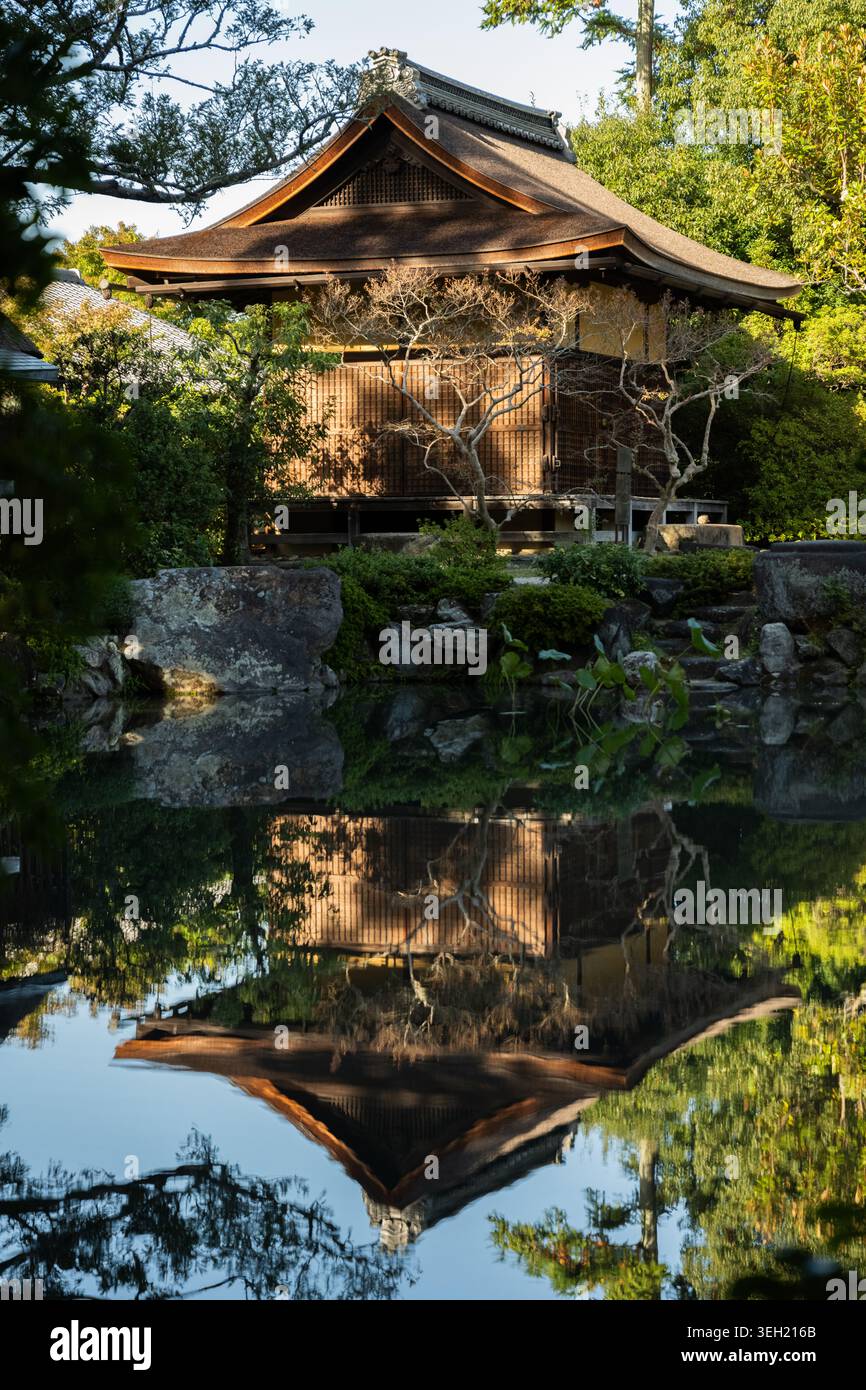 Maison de thé japonaise Chashitsu dans un jardin serein, donnant sur un étang calme qui reflète parfaitement la structure et la verdure environnante. Banque D'Images