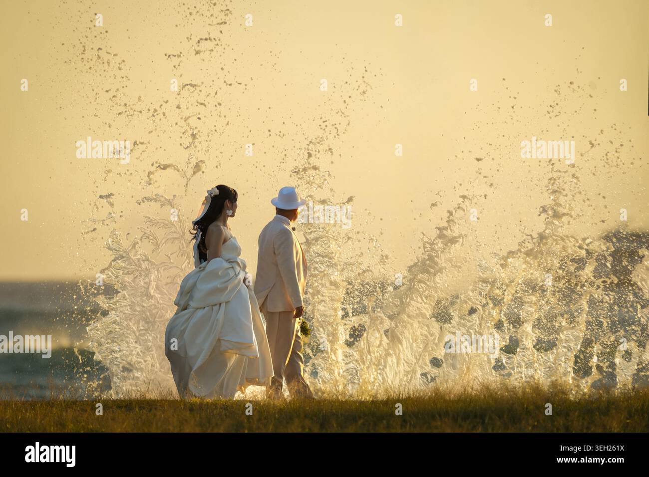 Mariée et mariée se tiennent ensemble à l'heure dorée surplombant l'océan avec des vagues se brisant contre le mur de jetée Banque D'Images
