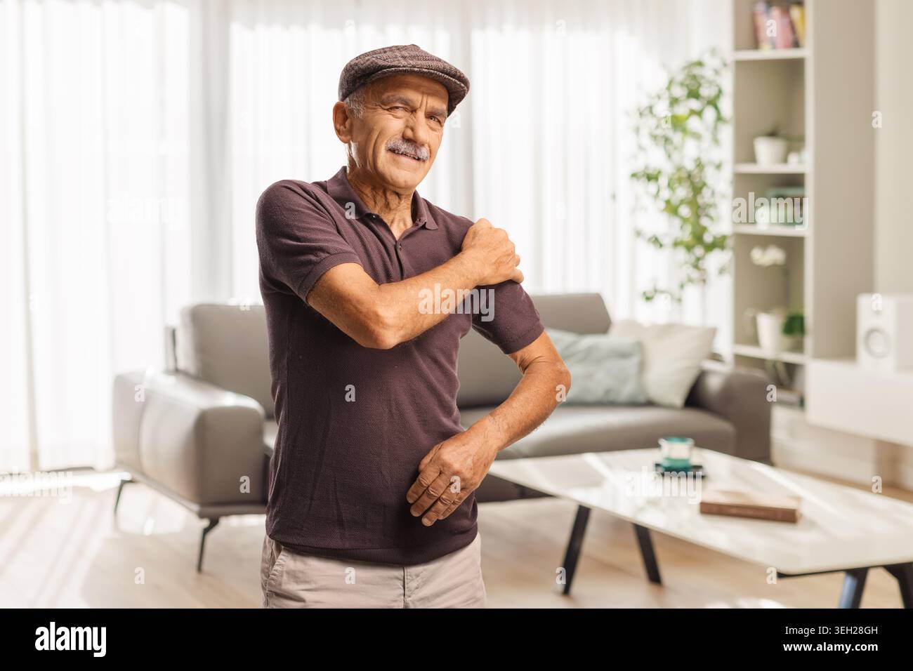 Homme âgé à la maison tenant son épaule dans la douleur Banque D'Images