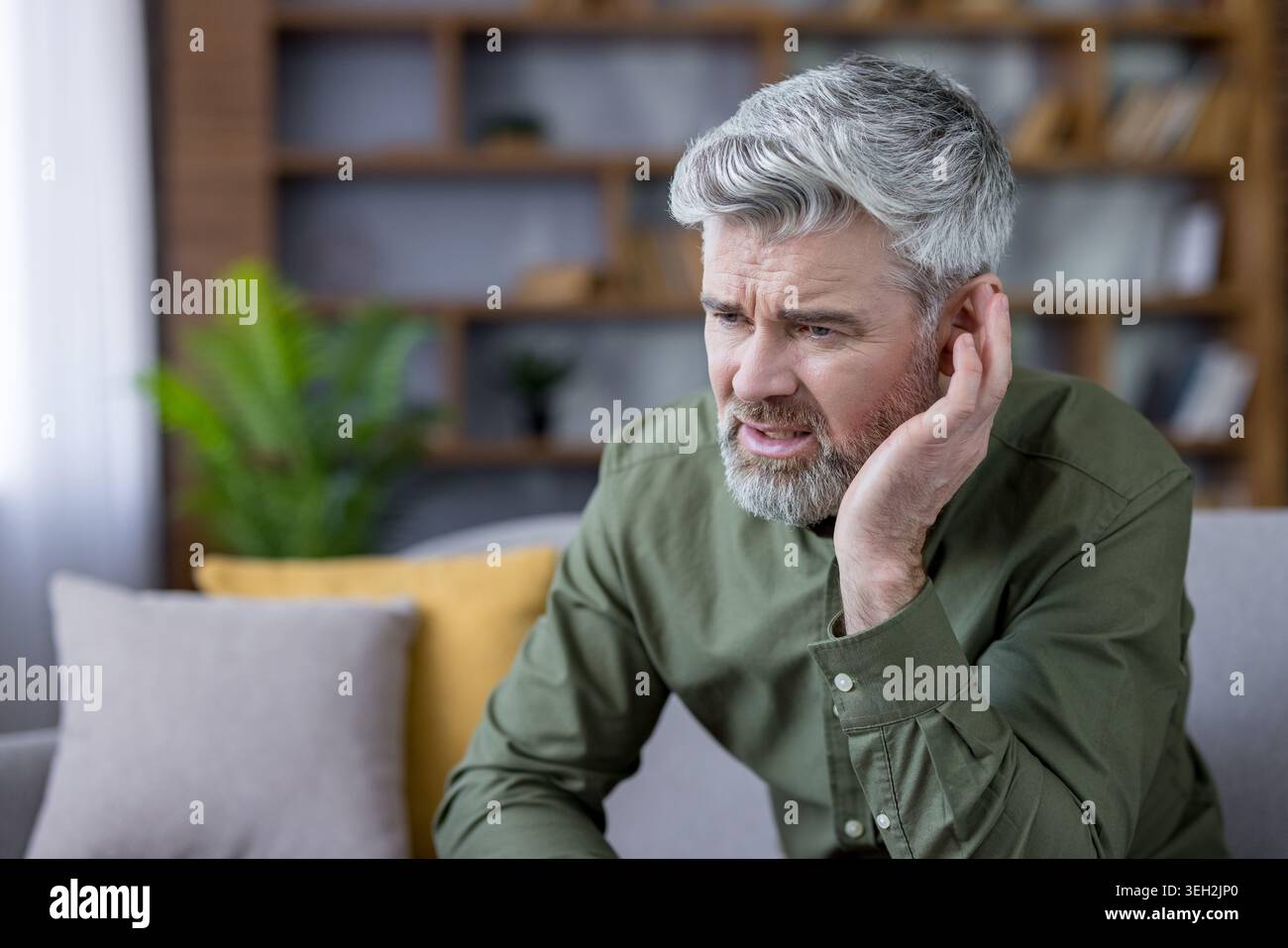 Homme mûr touchant son oreille avec une expression angoissée, souffrant d'un problème de santé tel qu'une perte auditive, une surdité, des douleurs auriculaires ou des acouphènes, éprouvant de l'inconfort et de la difficulté à entendre Banque D'Images