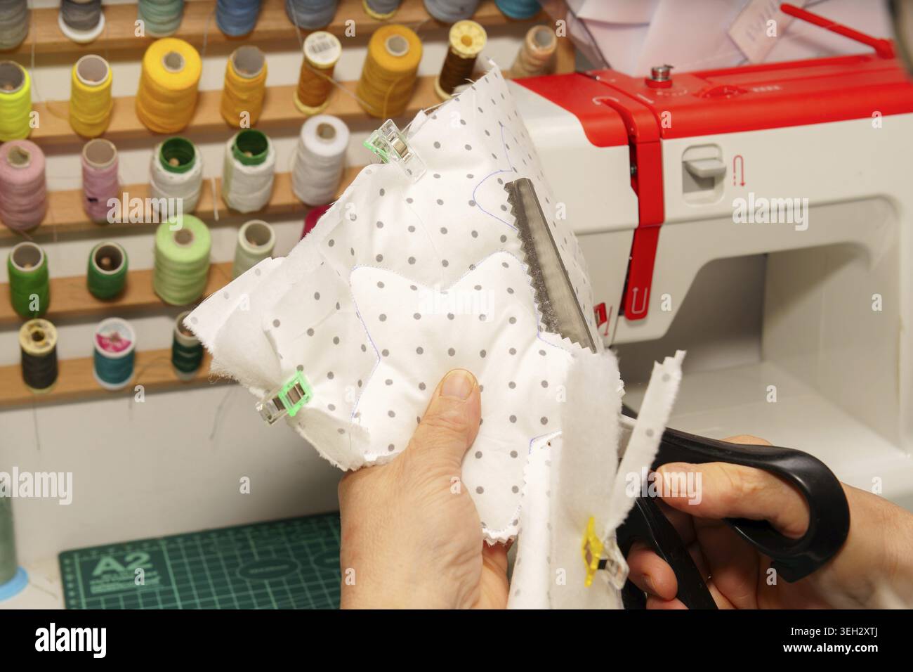 Personne fabriquant un article textile, en utilisant des ciseaux pour couper le tissu. Une machine à coudre et des fils colorés sont visibles en arrière-plan Banque D'Images