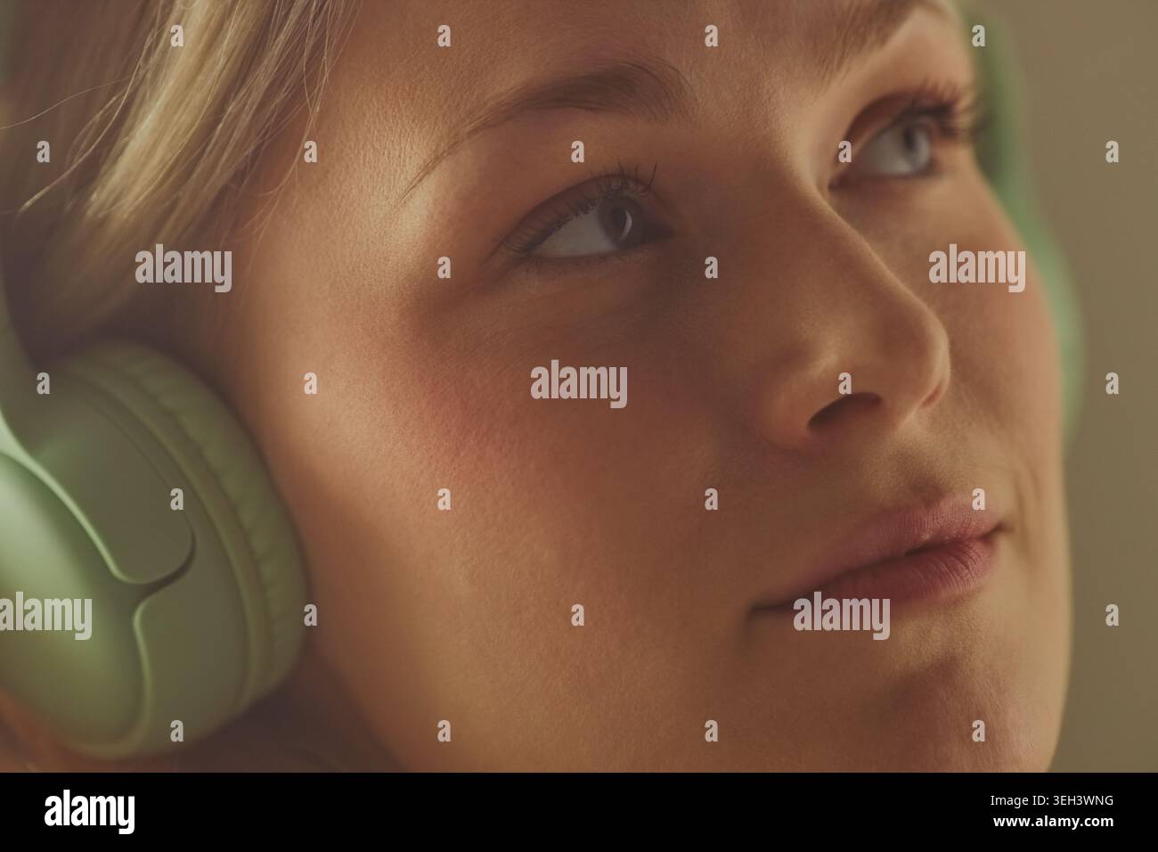 Gros plan d'une adolescente cente caucasienne portant des écouteurs, écoutant et regardant loin, suggérant la concentration et la relaxation. Utile pour le streaming de musique, l'apprentissage audio, le marketing de bien-être Banque D'Images