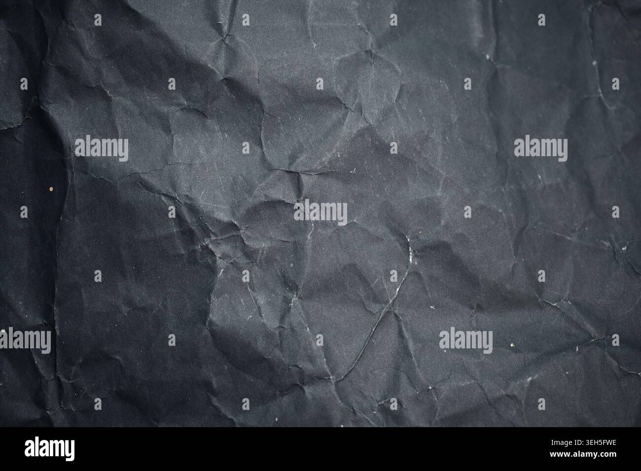 Texture de papier noir froissé en gros plan, montrant des plis sombres, des rainures, des plis rugueux et de petites marques de poussière comme fond abstrait grunge Banque D'Images