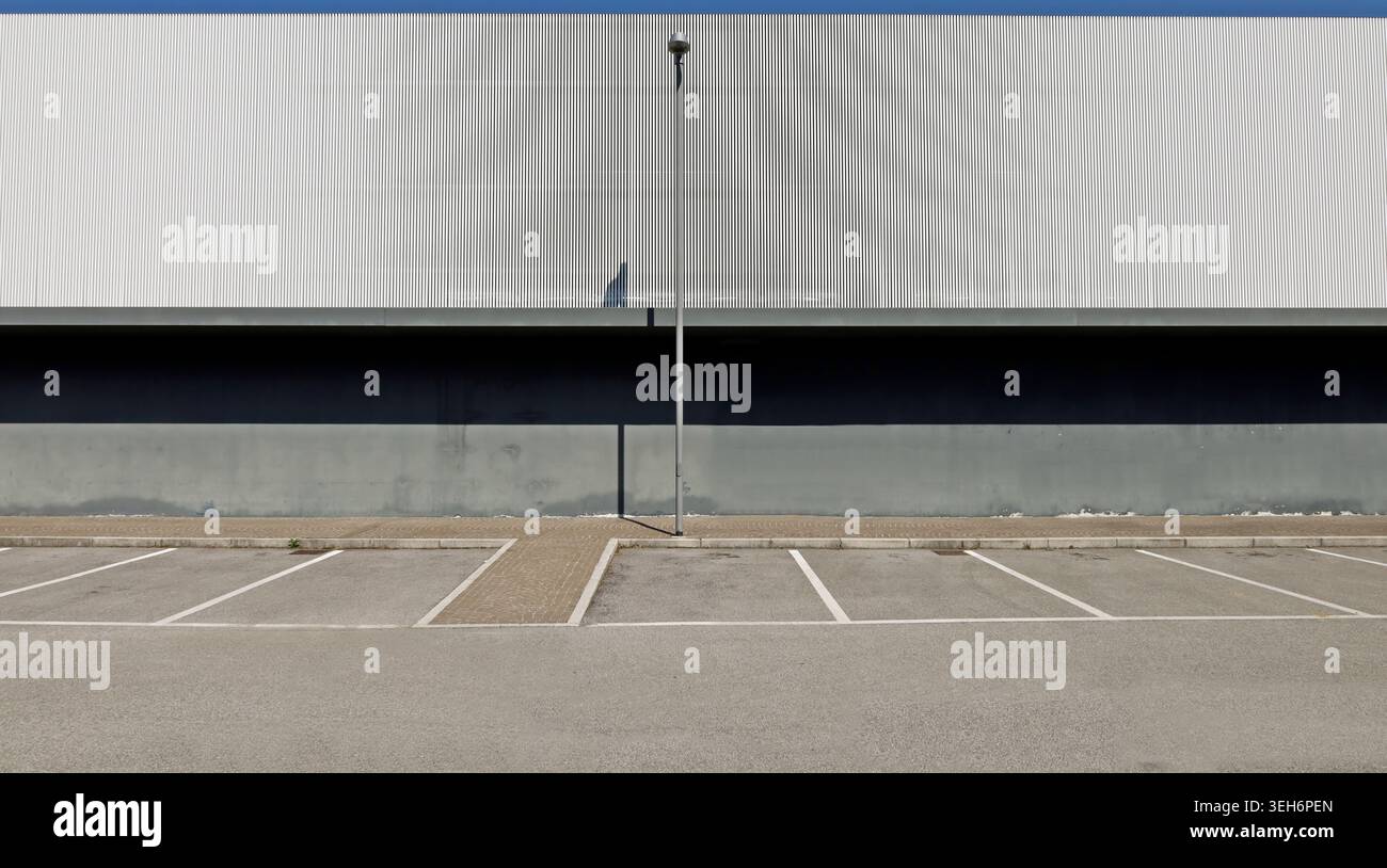 Mur extérieur en béton gris dans la partie inférieure et revêtement en aluminium dans la partie supérieure, avec un lampadaire. Porphyre trottoir, parking et rue Banque D'Images