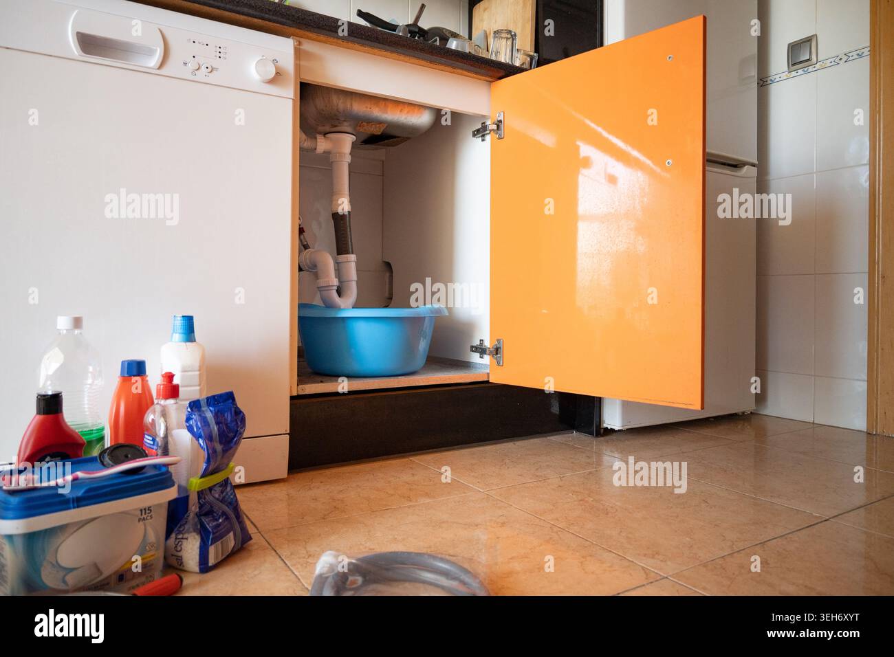 Les tuyaux d'évier de cuisine fuient l'eau dans un seau bleu, nécessitant une réparation Banque D'Images