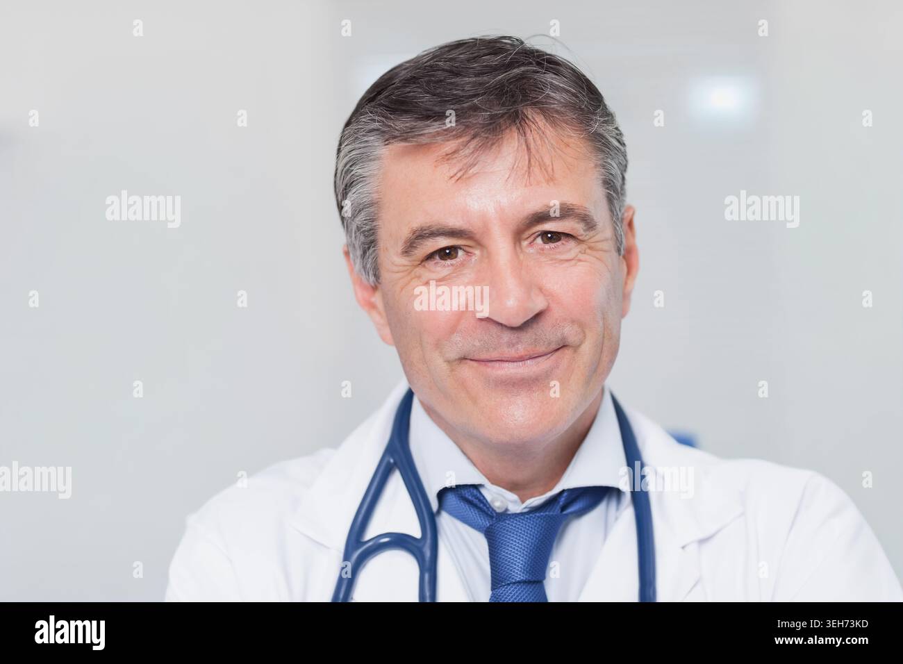 Souriant et regardant la caméra, médecin masculin mature portant une blouse de laboratoire, cravate bleue, stéthoscope en clinique Banque D'Images
