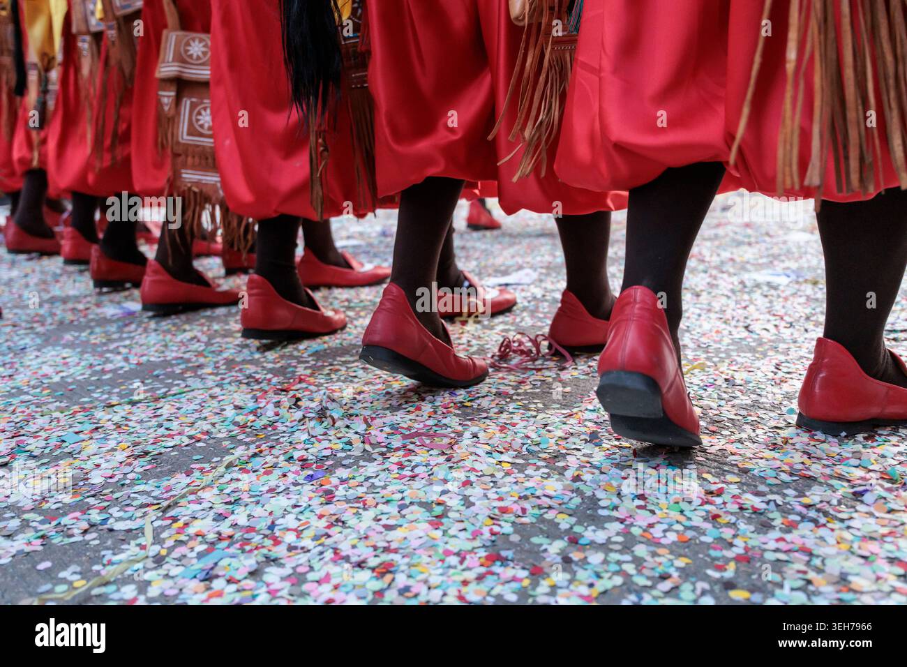 Gros plan de pieds marchant avec des chaussures rouges sur un terrain couvert de confettis dans Traditional Parade Banque D'Images