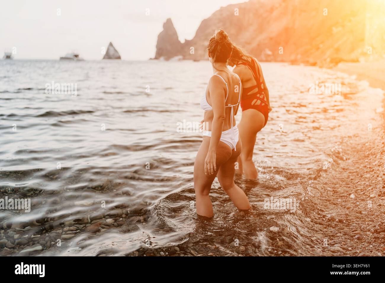 Femmes, plage, océan. Deux femmes debout dans l'eau peu profonde à une plage de galets profitant de vacances d'été au bord de la mer Banque D'Images