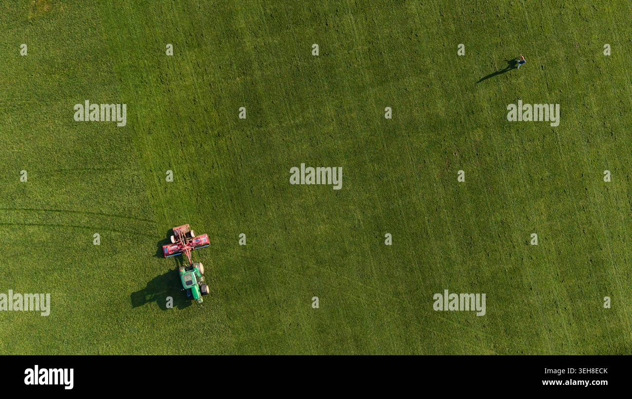 Drone vue de dessus d'un tracteur coupant l'herbe sur un terrain vert ouvert avec une personne à proximité. Banque D'Images
