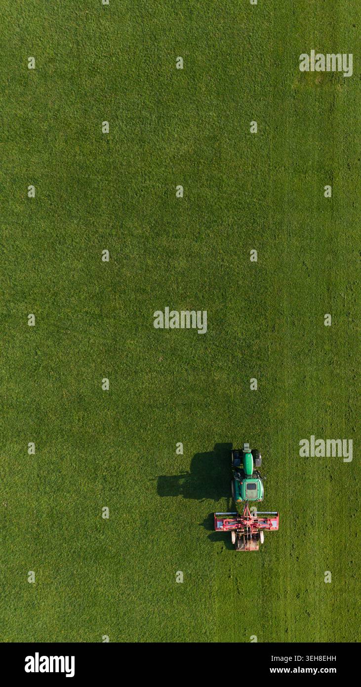 Vue aérienne verticale de dessus d'un tracteur fauchant une pelouse verte dans un parc Banque D'Images
