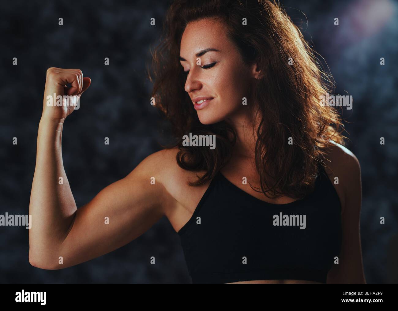 Femme brune en débardeur noir montrant bicep et sourire Banque D'Images