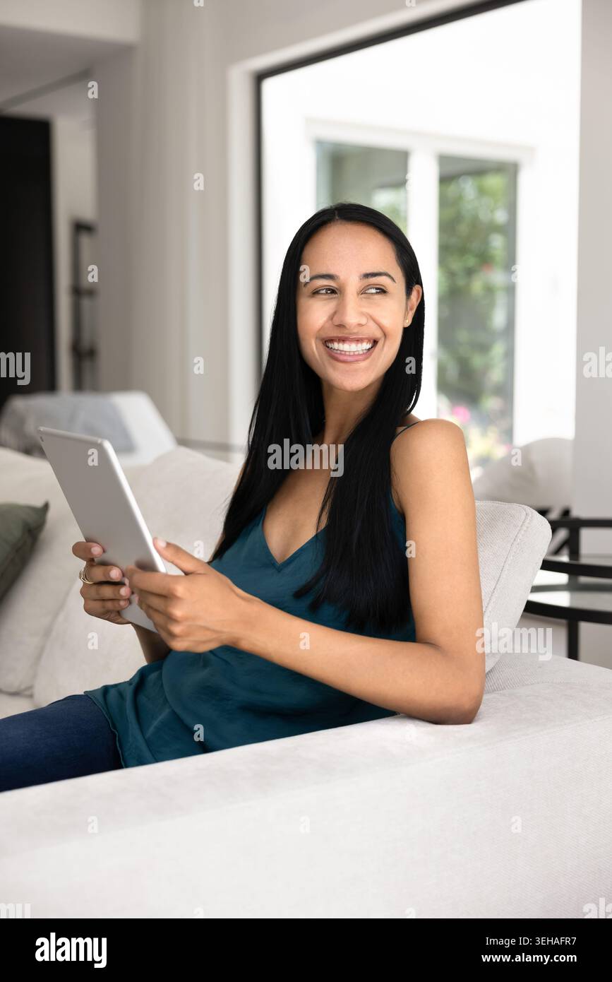Joyeuse femme néo-zélandaise se relaxant sur un canapé avec tablette Banque D'Images