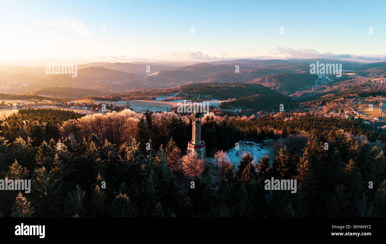 La tour de guet Stepanka se dresse dans les montagnes de Jizera pendant l'hiver. Le soleil se couche derrière des collines lointaines, projetant la lumière sur les arbres givrés et les s. Banque D'Images
