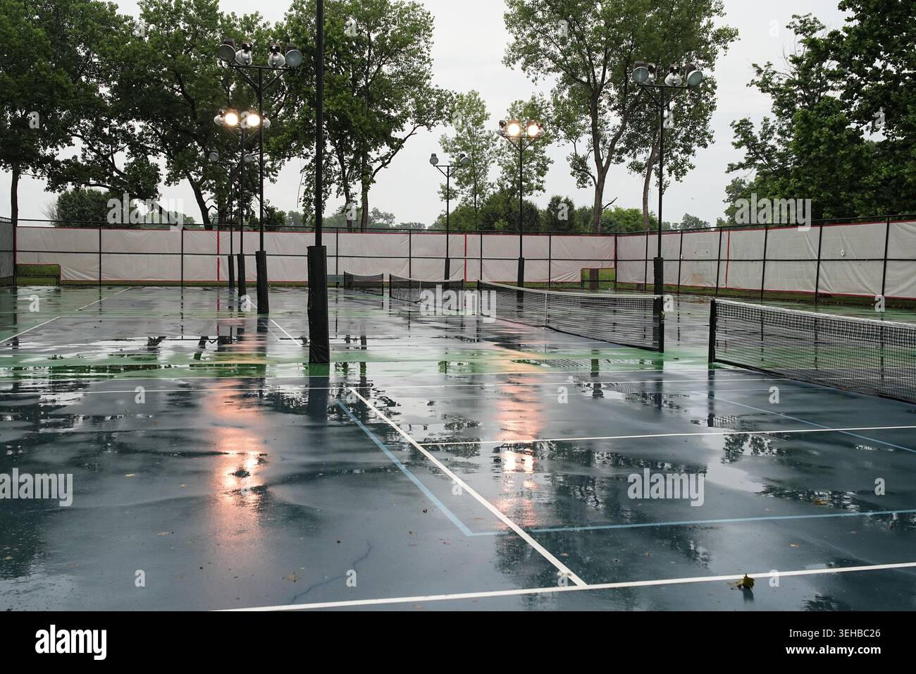Courts de tennis un jour de pluie, avec des reflets des lumières d'inondation dans l'eau. Banque D'Images