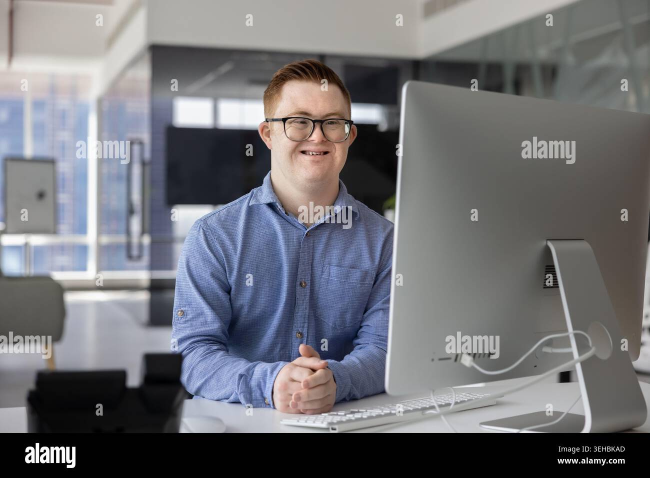 Homme avec le syndrome de Down assis au bureau avec l'ordinateur, portrait Banque D'Images