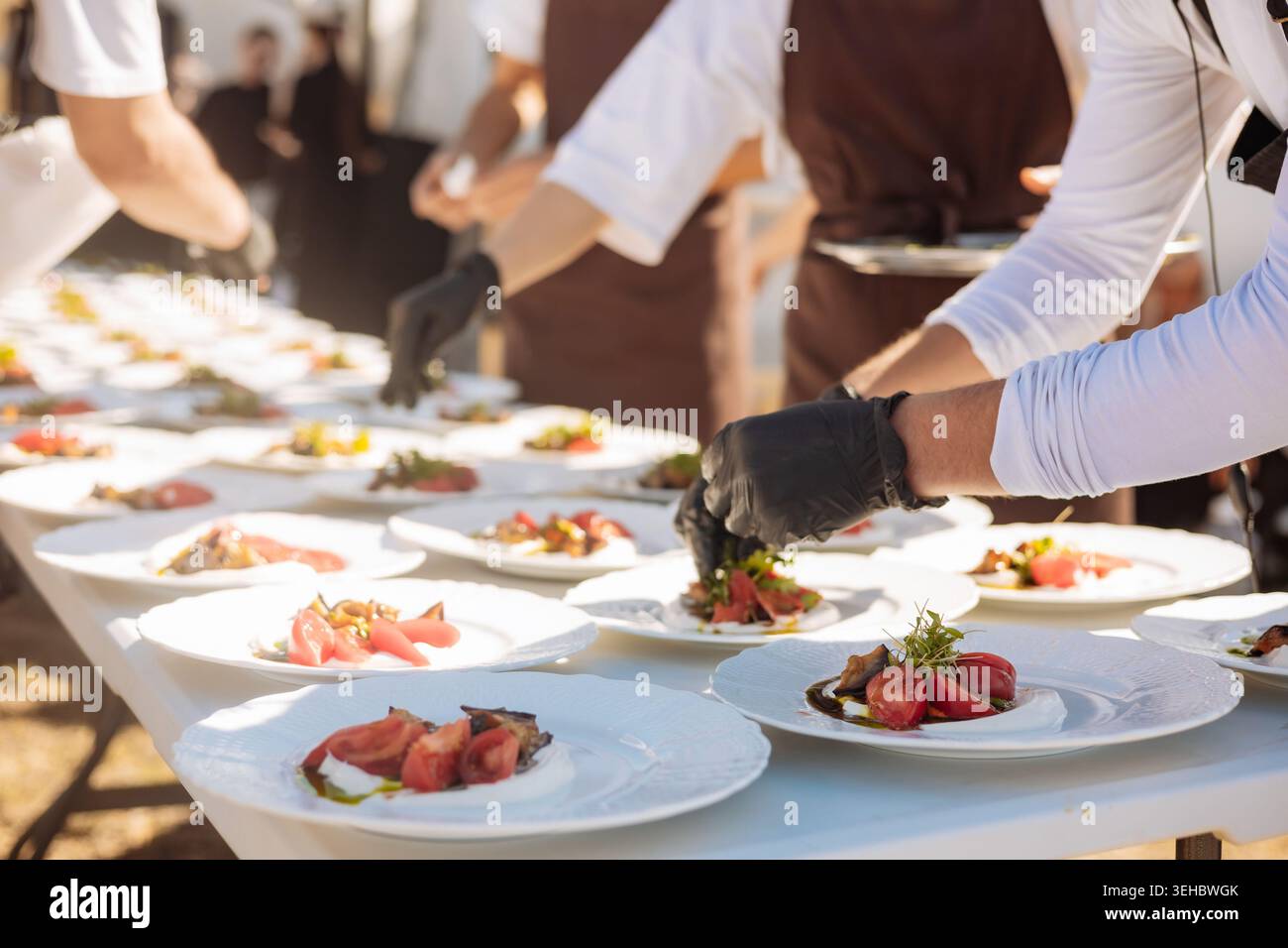 L'équipe de restauration dans les tabliers dispose des ingrédients frais dans les assiettes pendant la préparation de l'événement. Parfait pour le contenu d'entreprise d'hospitalité, véhiculant la profession Banque D'Images