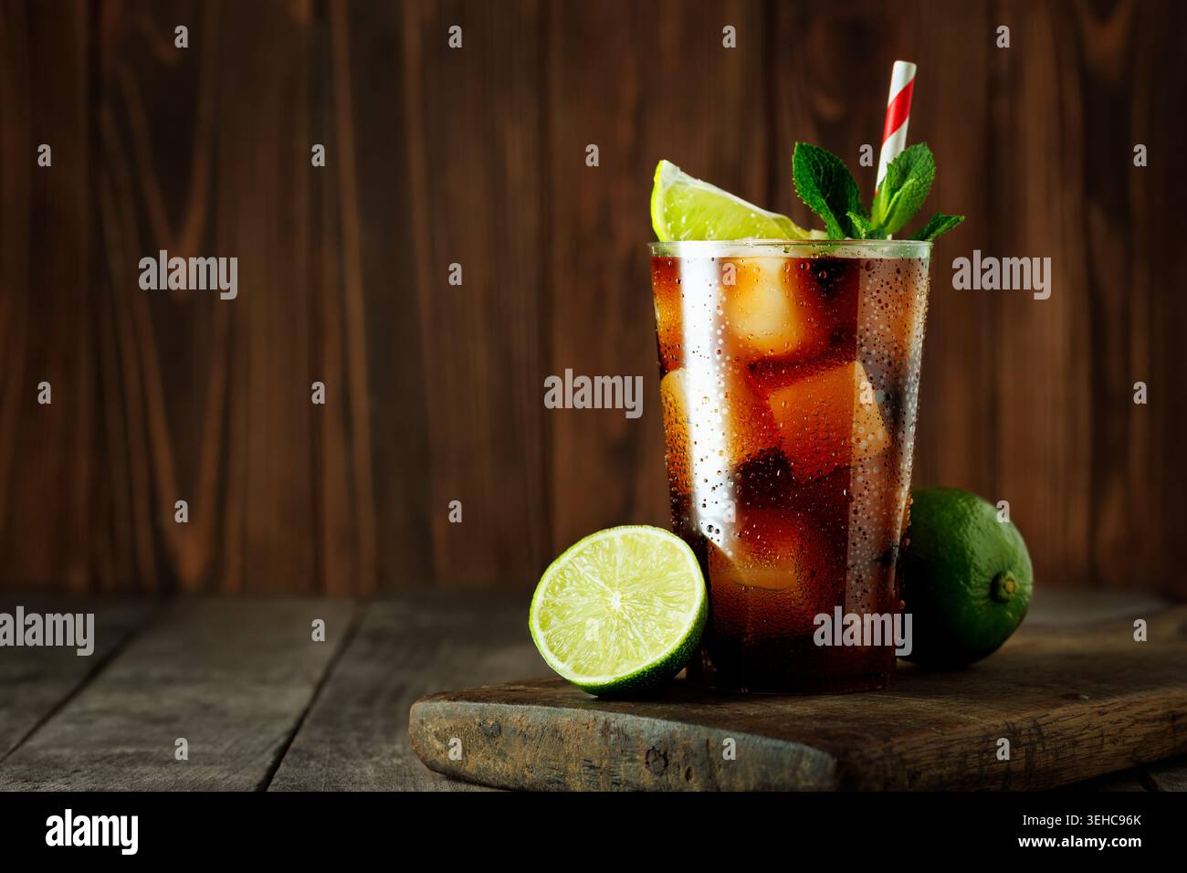 Cuba libre Drink, avec du cola, du rhum, des glaçons, du citron vert et des feuilles de menthe fraîche, debout sur une surface en bois avec un fond rustique Banque D'Images