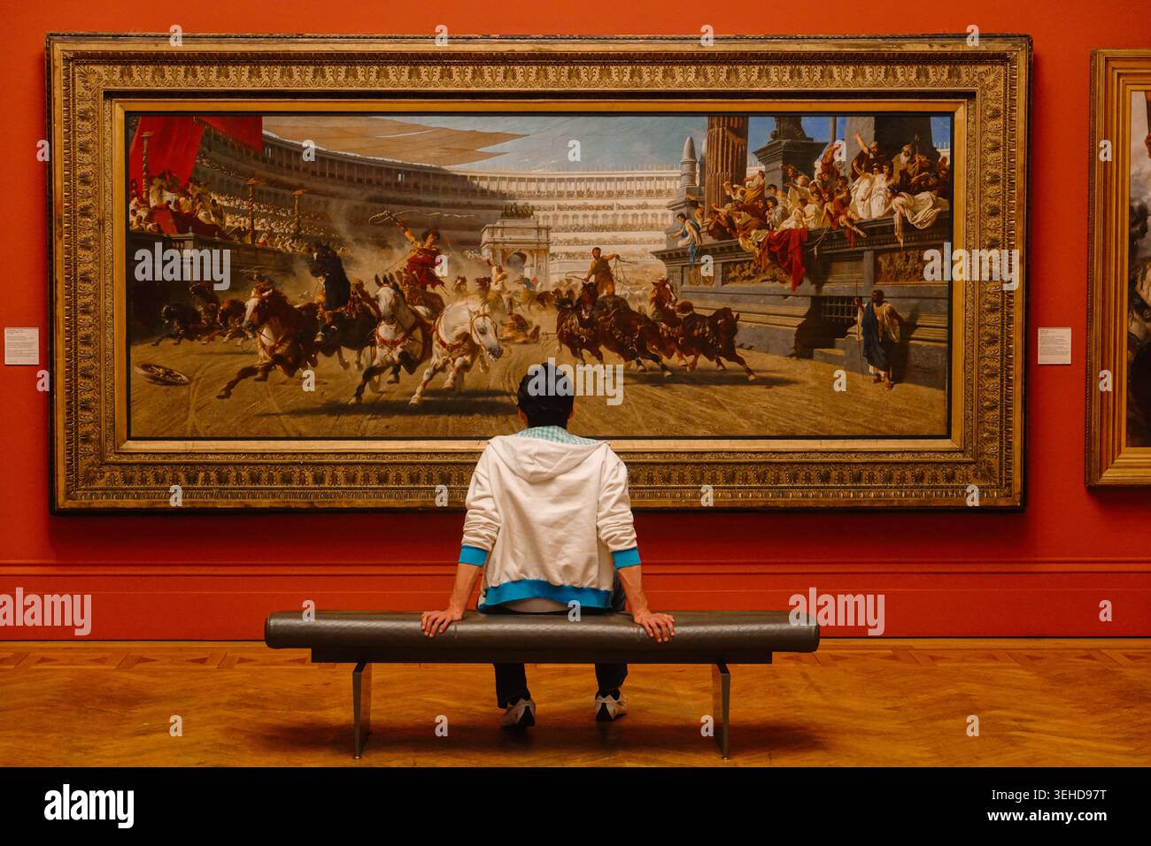 Un visiteur assis sur un banc regarde la peinture monumentale d'Alexander von Wagner, la course au chariot, à la Manchester Art Gallery, Angleterre, Royaume-Uni Banque D'Images