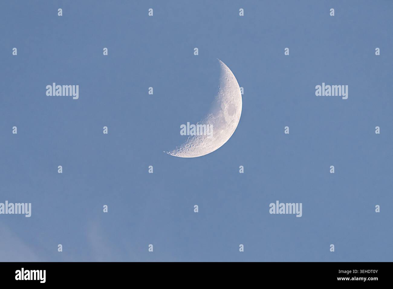 Ciel nocturne doux. Paisible croissant de lune reposant sous la canopée bleu pâle de nuages. Croissant de lune serein doucement illuminé contre le ciel bleu clair wi Banque D'Images
