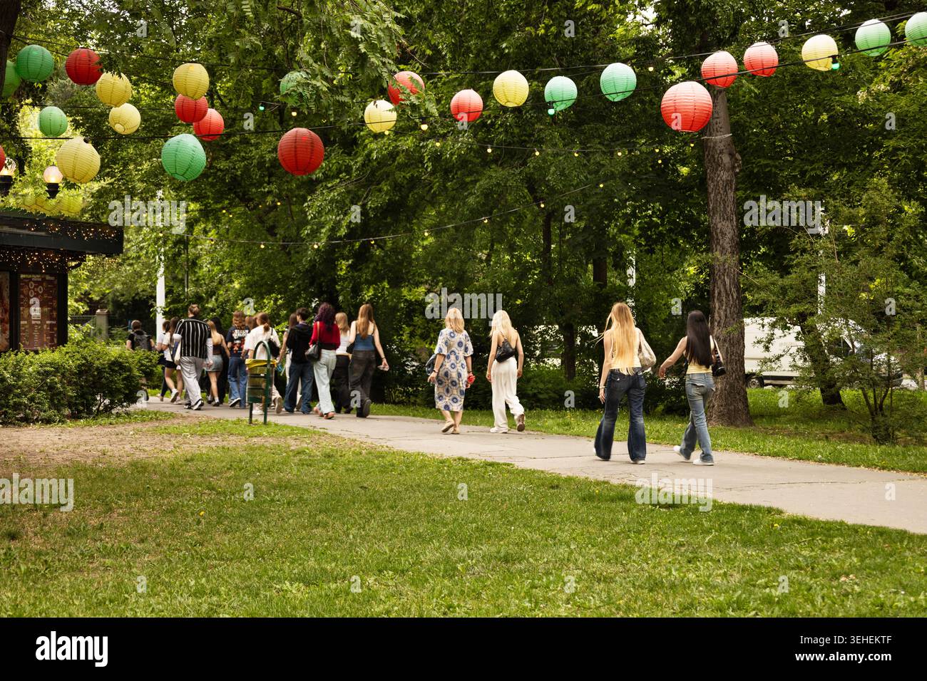 Touristes marchant sur un chemin de parc sous des lanternes suspendues décoratives. Banque D'Images