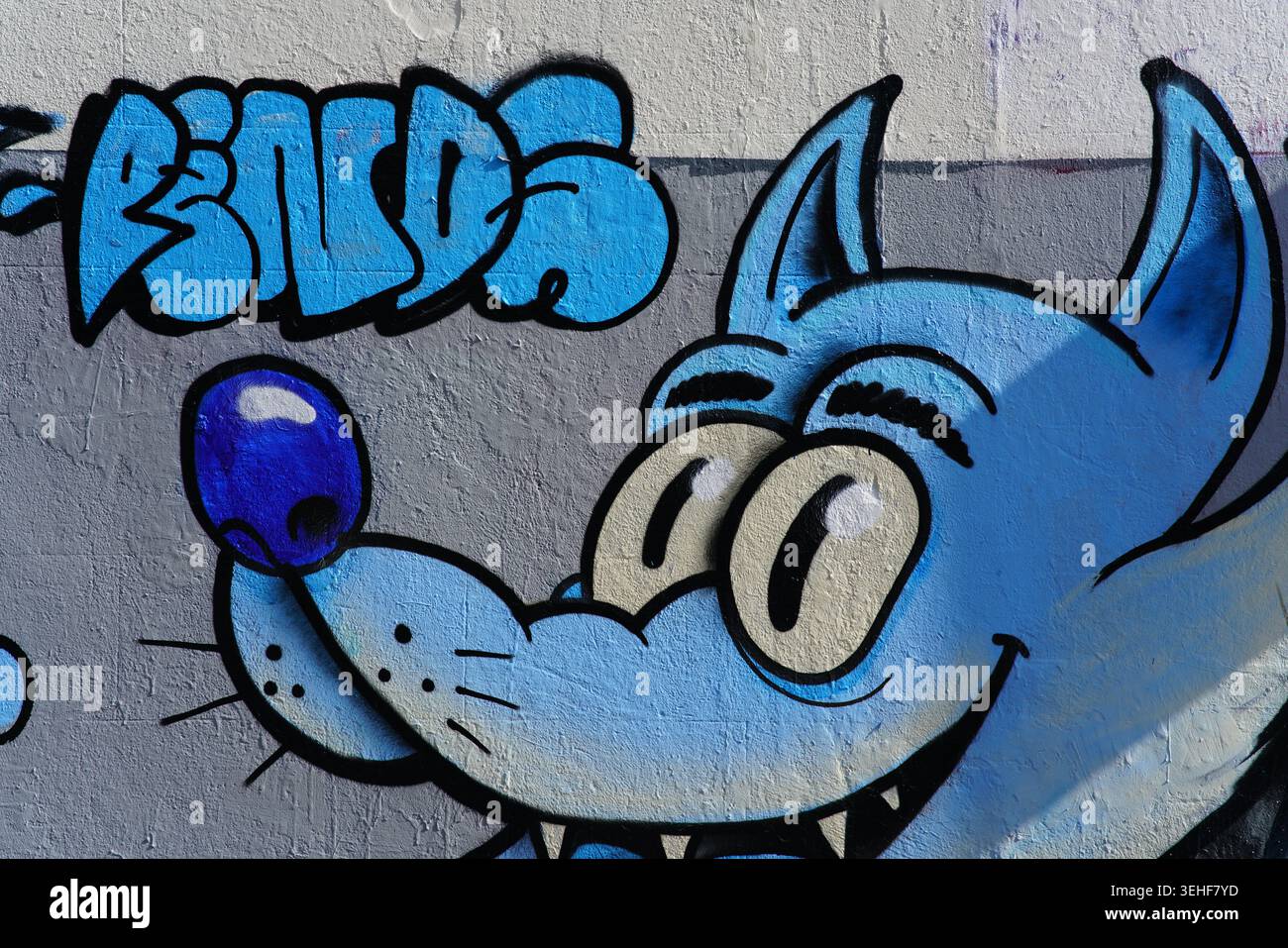 Loup de dessin animé bleu ludique avec de grands yeux expressifs et des dents acérées par l'artiste de rue Phat Chef vibrant graffiti murale sur un mur à Brighton, en Angleterre. Banque D'Images