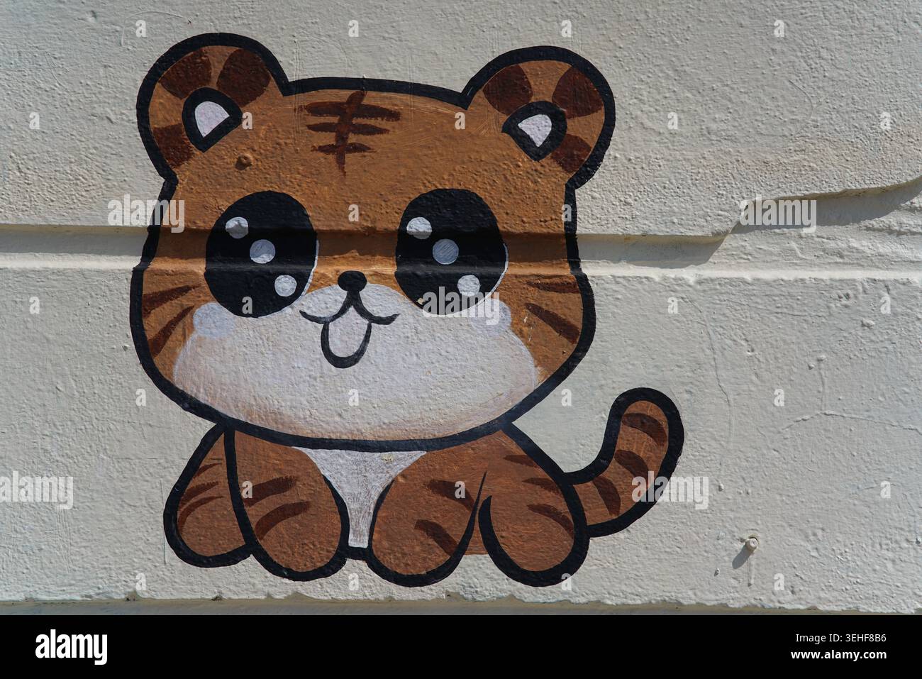 Adorable tigre de dessin animé avec de grands yeux étincelants et une expression ludique murale mignonne art de rue de style kawaii peinte sur un mur blanc à Brighton, en Angleterre. Banque D'Images