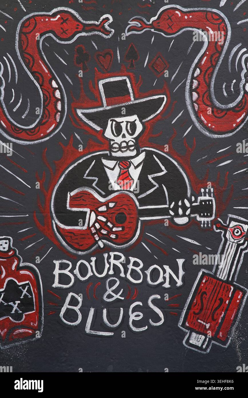 Squelette de cow-boy jouant de la guitare rouge entouré de serpents rouges et de bouteilles de poison avec texte « Bourbon & Blues » murale d'art de rue audacieux à Brighton, en Angleterre. Banque D'Images