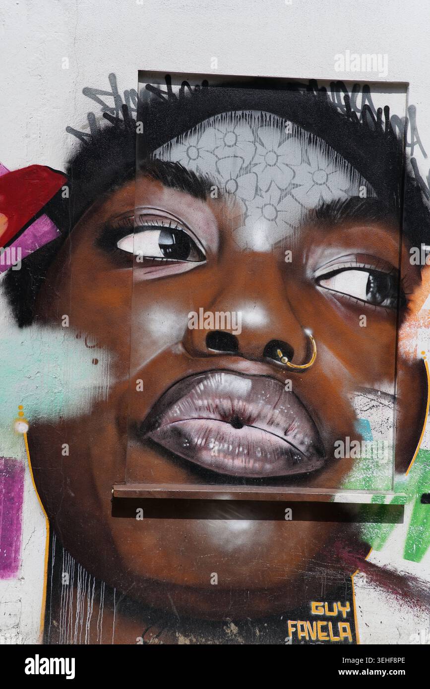 Puissant portrait réaliste d'une jeune femme noire avec anneau de nez et regard latéral intense par l'artiste de rue Guy Favela sur un mur à Brighton, en Angleterre Banque D'Images