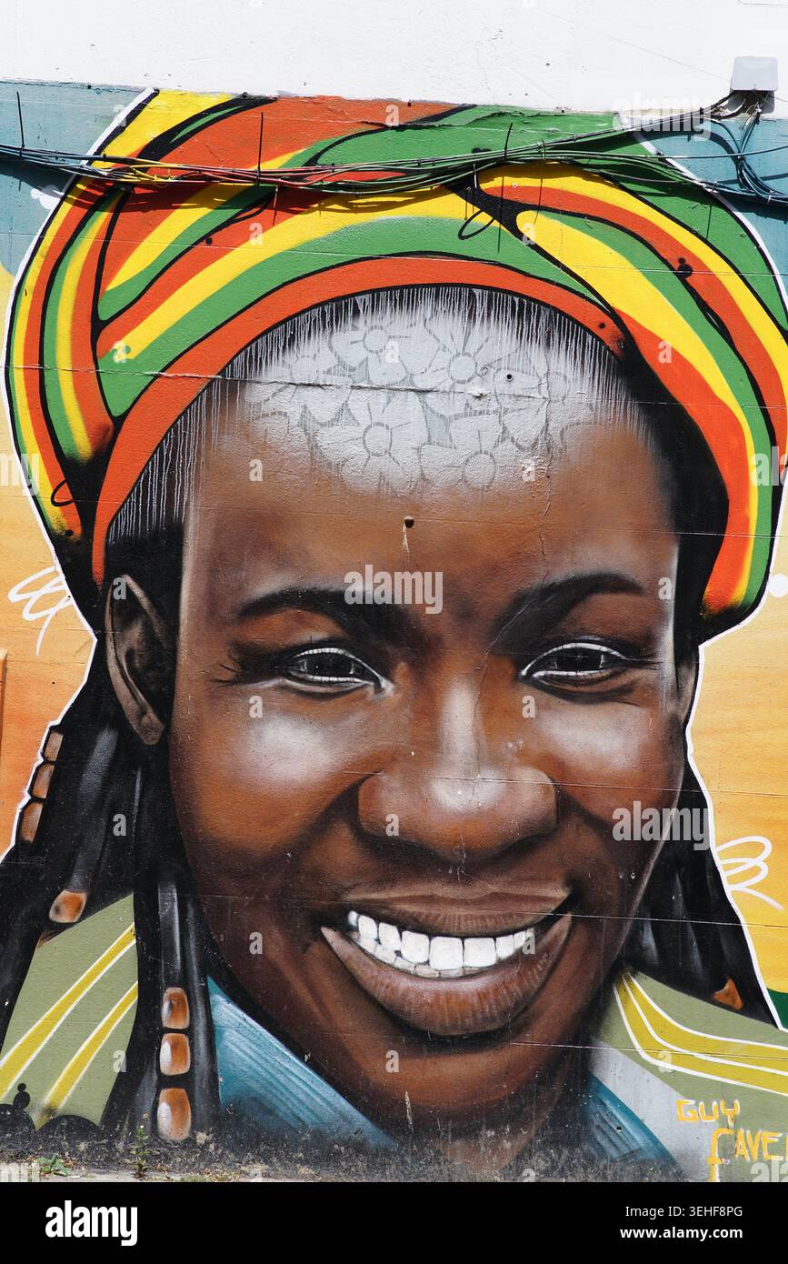 Portrait joyeux et souriant d'une jeune femme noire portant un couvre-tête de couleur Rasta éclatante par l'artiste de rue Guy Favela sur un mur à Brighton, en Angleterre. Banque D'Images
