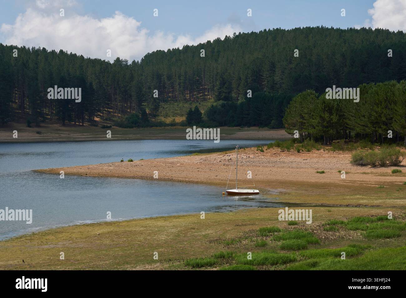 Petit voilier amarré dans les eaux peu profondes près d'un rivage aride avec une forêt de pins dense sur le versant de la montagne sous un ciel bleu d'été Banque D'Images