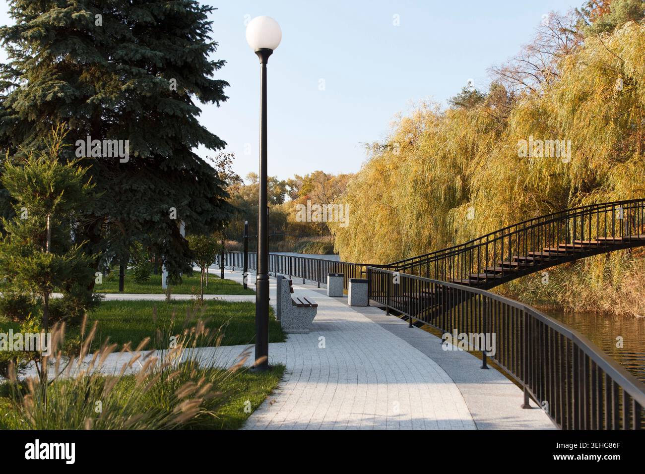 Un parc serein avec un sentier sinueux, un pont en bois et des arbres luxuriants avec feuillage d'automne. Un lampadaire se tient le long du chemin, améliorant le tranqui Banque D'Images