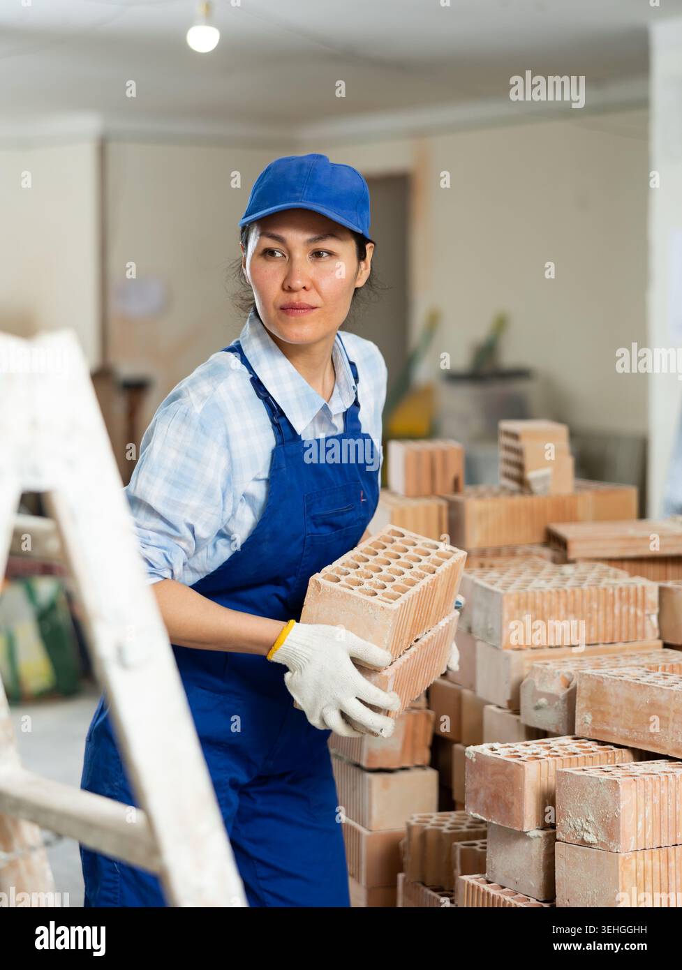 Femme constructeur transportant des briques d'argile creuses et les mettant sur la pile de briques Banque D'Images