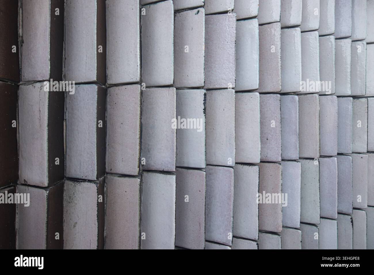 Vue rapprochée d'un mur architectural moderne fait de carreaux de céramique incurvés de couleurs blanche, grise et marron, mettant en valeur des motifs géométriques répétitifs. Banque D'Images