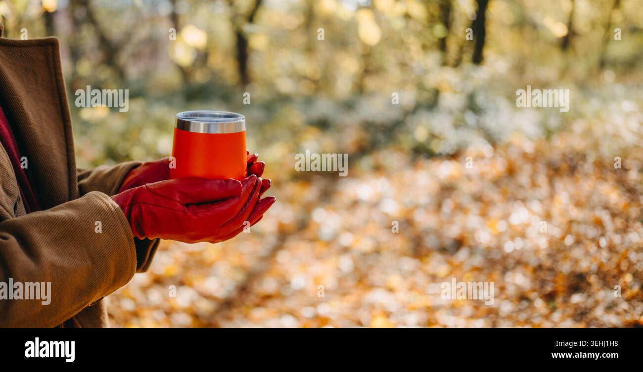 Les mains tiennent le récipient de boisson isolé à l'extérieur avec un fond d'automne flou. Profitez d'une belle matinée d'automne, d'une marque de style de vie par temps froid Banque D'Images