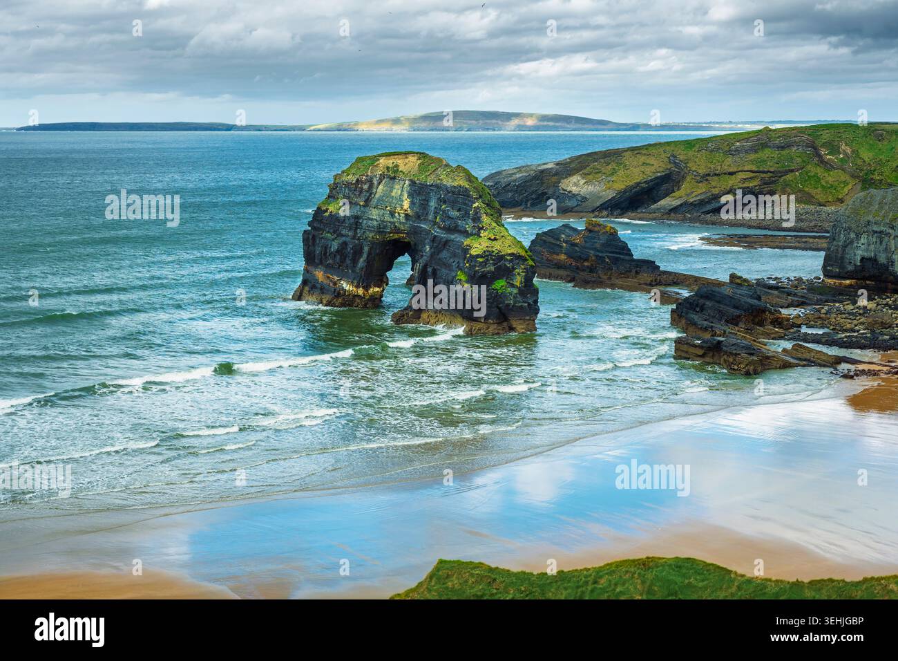 Vue côtière panoramique de l'arc en pierre naturelle de la pile de mer Virgin Rock à Nuns Beach avec des reflets de nuages sur le sable et l'eau turquoise, Kerry Irlande. Banque D'Images