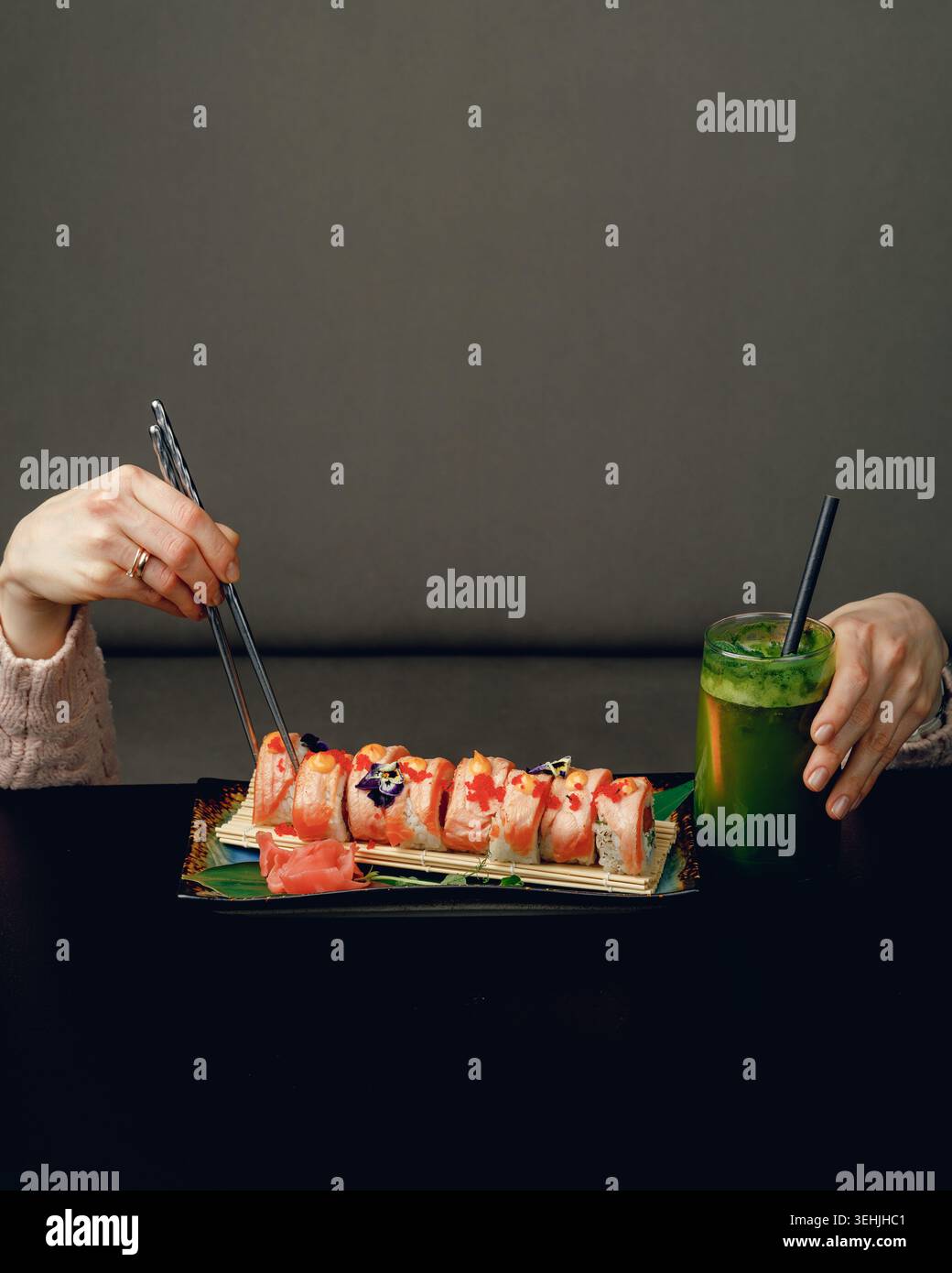 Une fille sous une table avec des baguettes sur la table mange des sushis et boit un cocktail. créatif, publicité, place pour le texte Banque D'Images